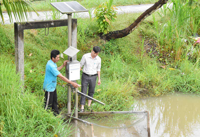 Nông dân Thạch Rên (bên trái) cùng cán bộ khuyến nông kiểm tra độ mặn để dẫn nước vào kênh bê tông đưa vào đồng ruộng.
