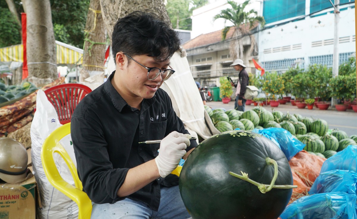 Bạn Trần Vũ Hoài An (phường Tân Ngãi) tỉ mỉ khắc chữ lên dưa hấu phục vụ thị trường Tết.